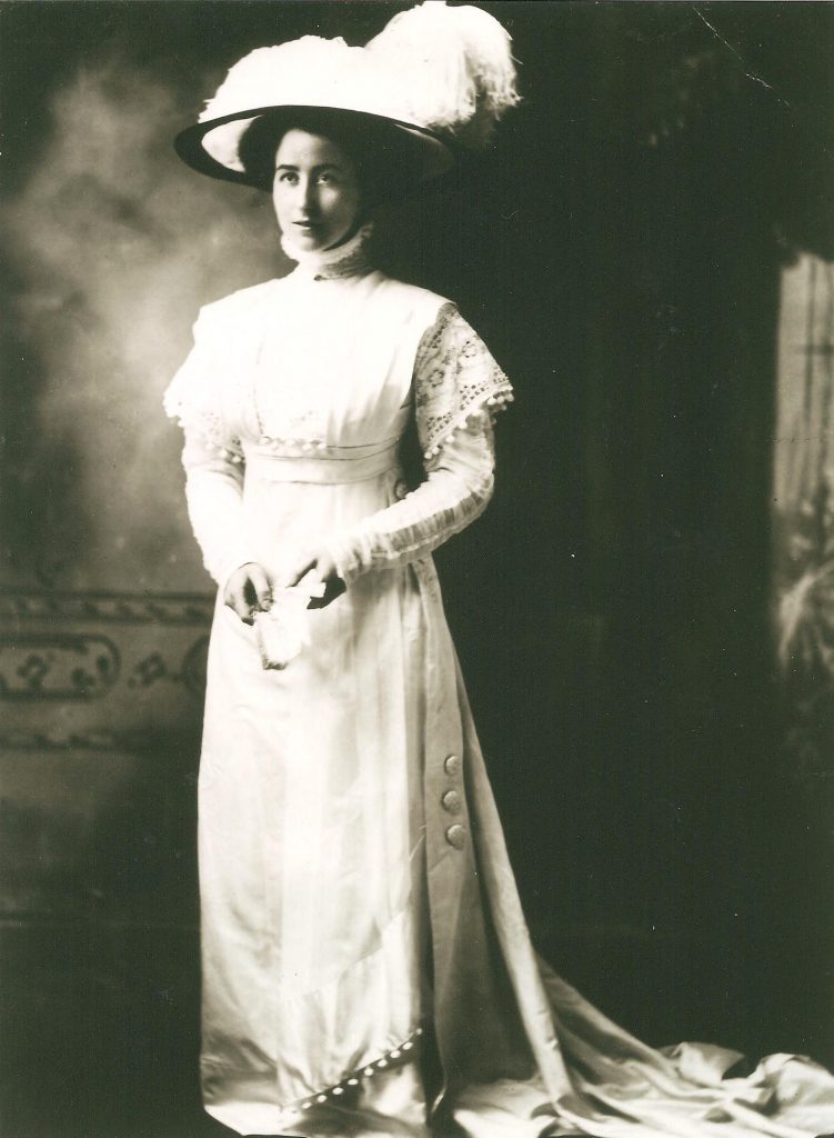 Bessie Heard Portrait in a white gown wearing a large hat with a big feather on top